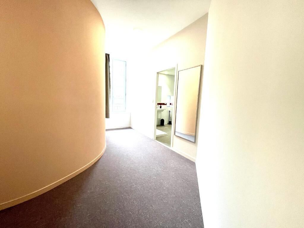 A hallway with a curved wall on the left, a door at the end, and a mirror on the right.