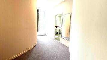 A hallway with a curved wall on the left, a door at the end, and a mirror on the right.