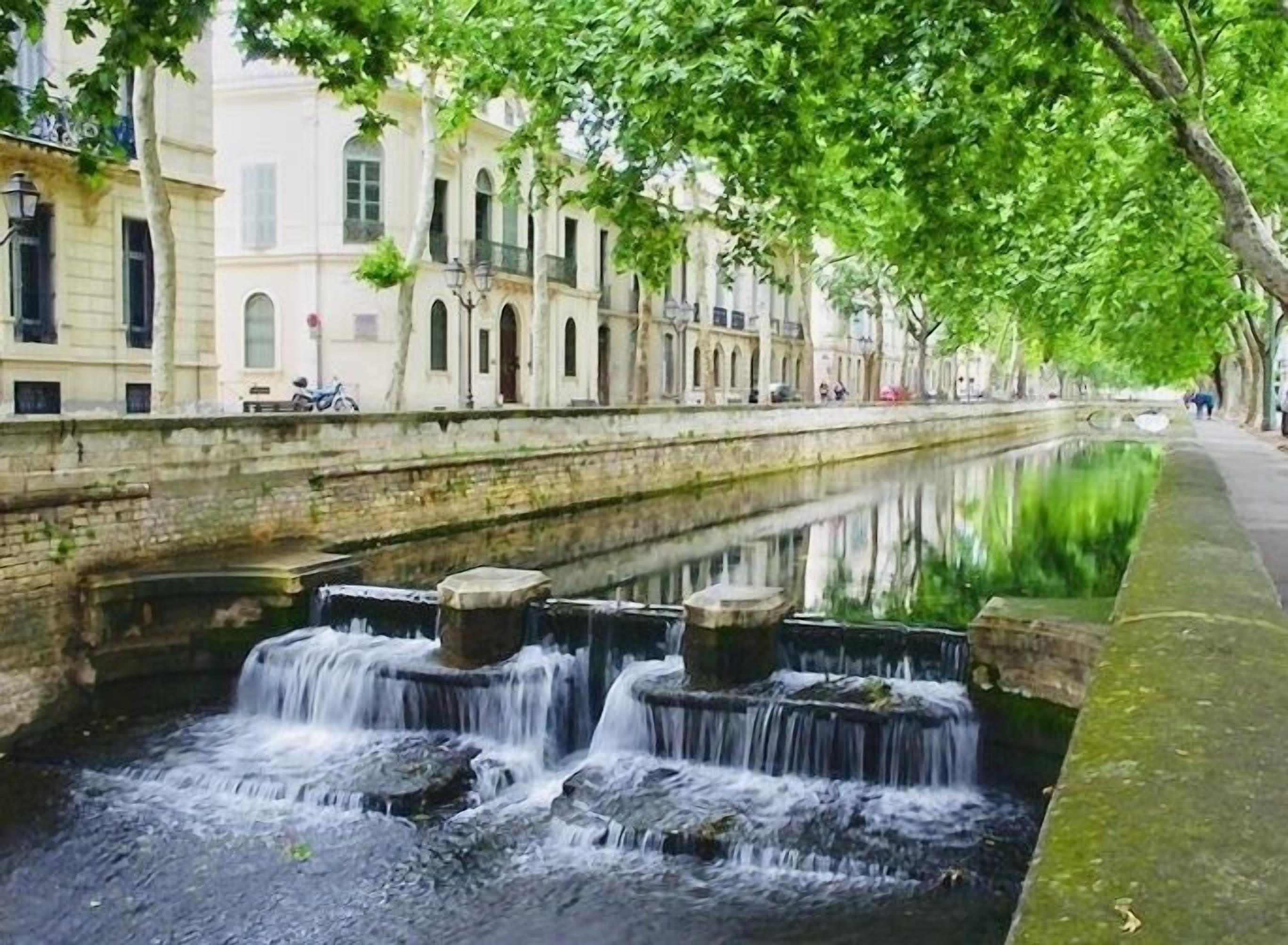 A canal with a small waterfall, surrounded by buildings and trees.