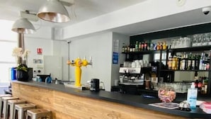 A bar area with a wooden counter, metal stools, and a yellow decorative figure. - Hostel Flamingo Nîmes Centre Gare (Nîmes)