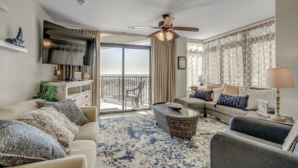 Ein geräumiges Wohnzimmer mit einem großen Flachbildfernseher, einem Deckenventilator und einem Balkon mit Blick.