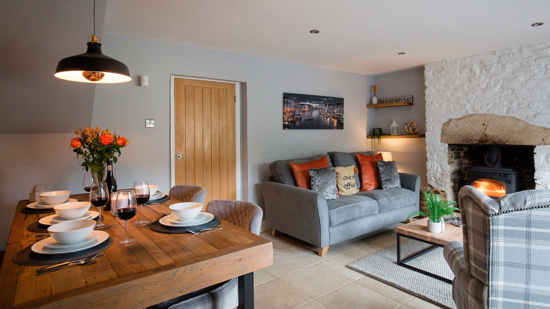 A cozy living room with a fireplace, a dining area with a wooden table set for a meal, and a comfortable sofa with cushions.