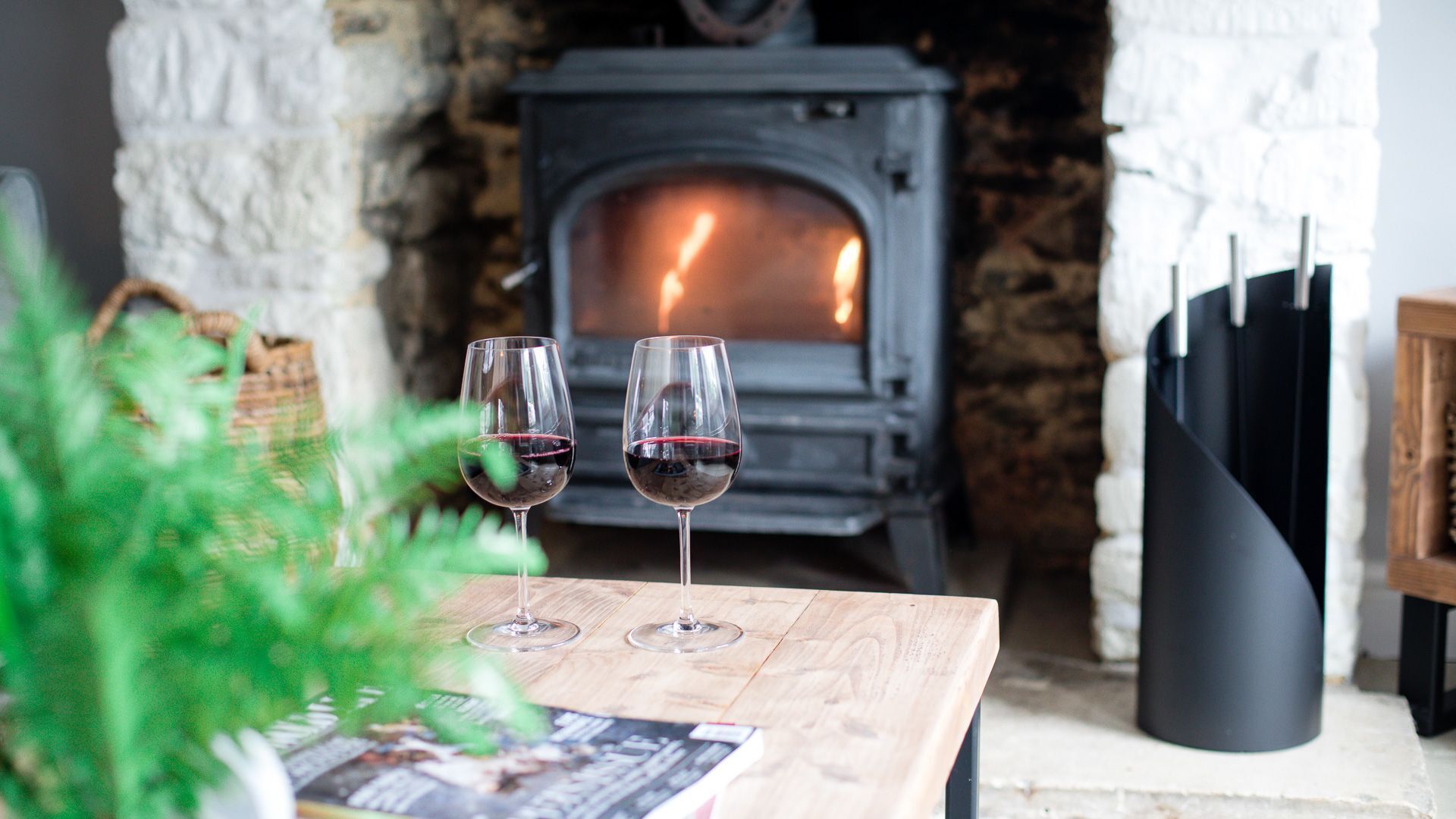 A cozy room with a stone fireplace, two wine glasses on a wooden table, and a potted plant.
