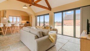A spacious living area with a sofa, dining table, and chairs, large windows with a view of the outside, and a kitchen area.