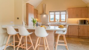 A modern kitchen with a central island, bar stools, wooden cabinets, a microwave, and a window with a view.