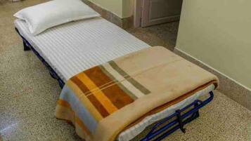 A single bed with a striped blanket and a pillow in a room with a tiled floor and a door in the background.