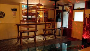 A bar area with wooden chairs, a dartboard, and a glass table.