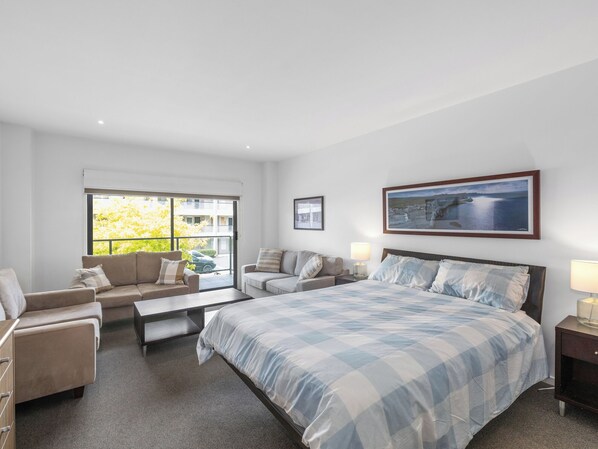 A modern bedroom with a large bed, two sofas, a coffee table, and a view of greenery outside.
