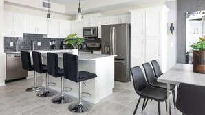 Une cuisine moderne avec des meubles blancs, un îlot central doté de tabourets, des appareils en acier inoxydable et un luminaire suspendu.