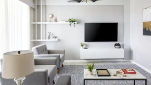 Un salon moderne avec un canapé gris, une table basse agrémentée d’objets décoratifs, un téléviseur fixé à un mur blanc et un lampadaire.