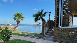 A wooden deck with a view of the sea, palm trees, and a boat docked nearby.