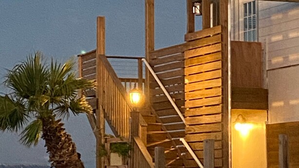 A wooden house with a staircase leading to a balcony, overlooking a body of water.