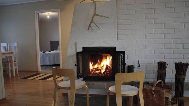 Ein Wohnzimmer mit Kamin, Holzstühlen, einem Essbereich und einer weißen Ziegelwand.