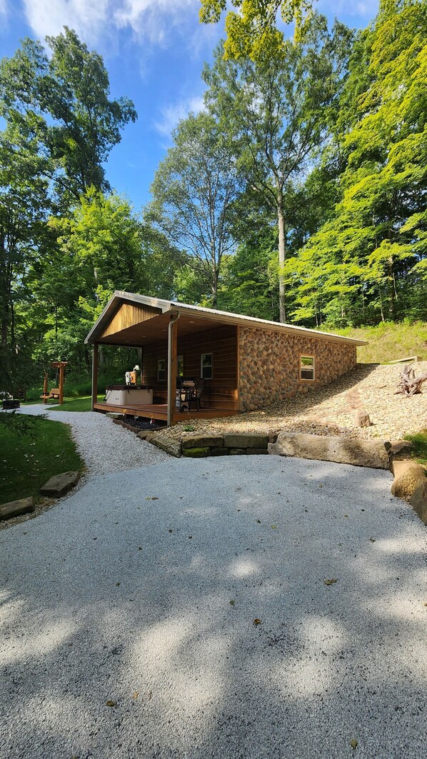 A rustic cabin with a stone exterior, a wooden porch, and a gravel driveway. - Hocking Hills (Buck Crossing Retreat) (Rockbridge)
