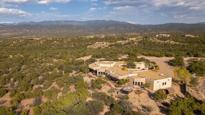 A large, modern house with a spacious outdoor area, surrounded by a desert landscape with mountains in the background.