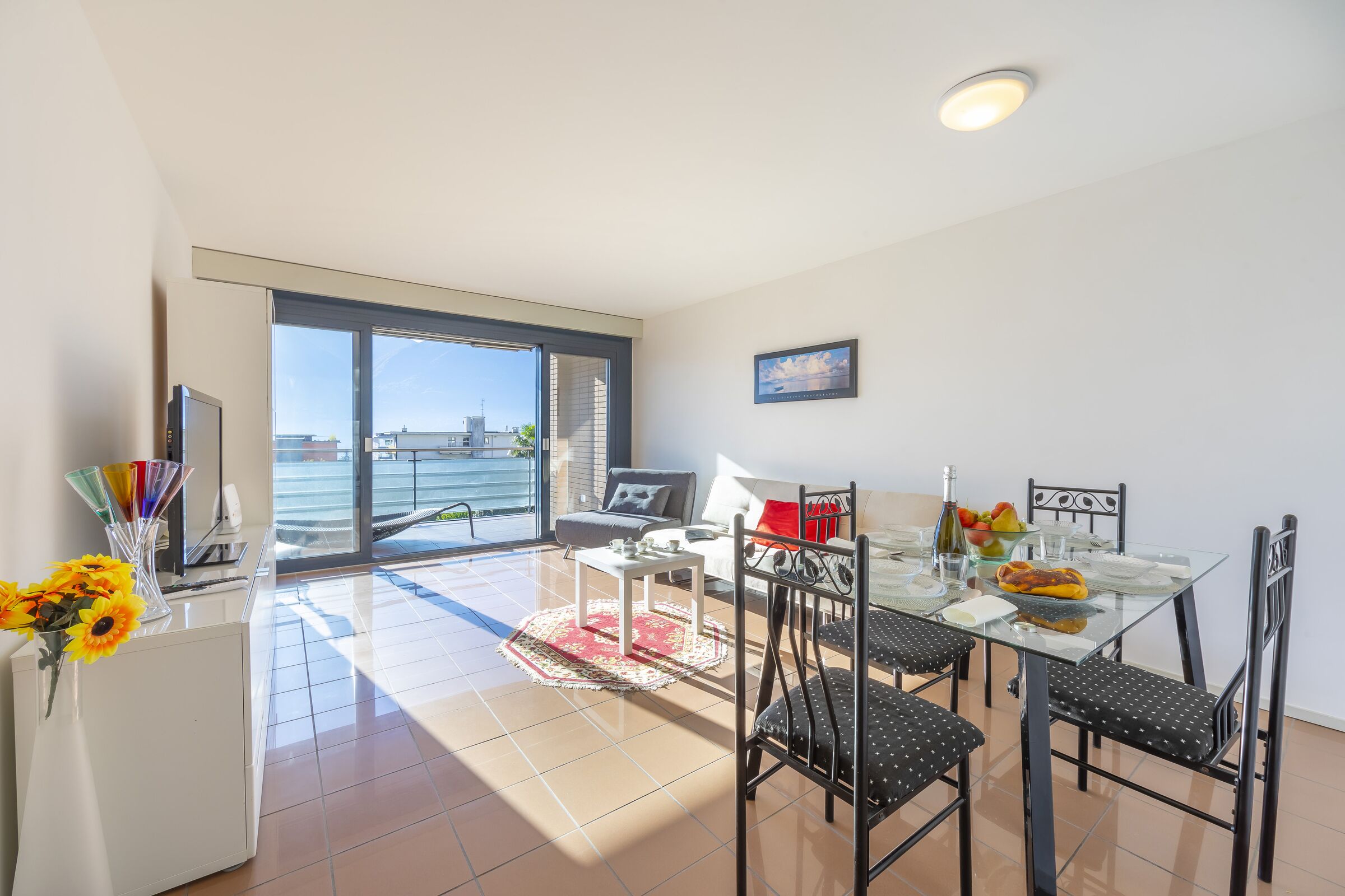 A modern dining area with a glass table, black chairs, and a view of the sea through large windows.