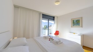 Habitación de hotel moderna con una cama grande, una silla roja, un escritorio y vistas a las montañas desde la ventana.