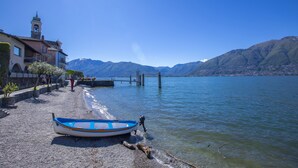 Un barco en una orilla pedregosa con montañas al fondo y un edificio con una torre.
