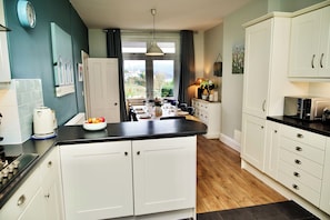 A modern kitchen with white cabinets, a black countertop, and a view of the outdoors through large windows.