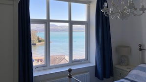 A bedroom with a large window offering a view of a lake and mountains.