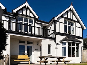 A two-story building with a balcony, a wooden bench, and a picnic table. - 5 Star Cottage, Sleeps 8, Amazing Sea & Mountain Views, Borth y Gest, Wales (Borth-y-Gest)