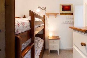 A bunk bed with a bedside table and a lamp, a white dresser, and a wall-mounted coat rack.