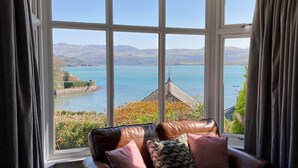 Quarto com uma grande janela que oferece vista para um lago e colinas ao longe.