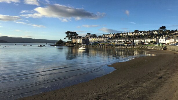 A coastal town with a sandy beach, calm water, and a row of houses along the shore.