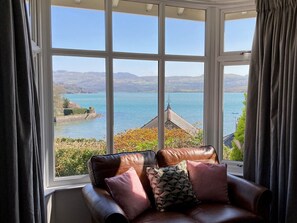 A room with a large window offering a view of a lake and distant hills. - Two neighbouring 5* Cottages (sleeps 16 in total) Amazing Sea & Mountain Views (Borth-y-Gest)