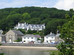 A coastal town with a prominent white building with multiple windows and a balcony, surrounded by lush green hills.