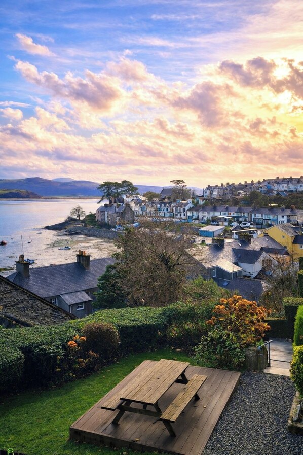 A coastal village with houses, a beach, and a picnic table in a garden.