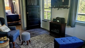 A cozy living room with a blue sofa, ottoman, and a television mounted on the wall.