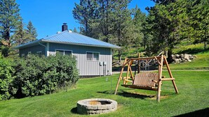 A house with a blue roof, a wooden swing set, and a stone fire pit in a grassy yard.
