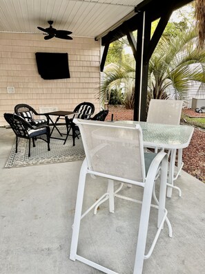 A covered patio area with a table and chairs, a ceiling fan, and a view of the outdoors including palm trees. - Ocean Lakes site 6013 beautiful 3 bedroom quiet street 2 carts available (Myrtle Beach)