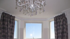 Um quarto com um amplo parapeito, duas poltronas estofadas, um candelabro e cortinas.