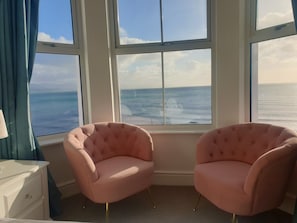 Quarto com duas poltronas cor-de-rosa com detalhes em tufos, viradas para uma grande janela com vista para o mar.