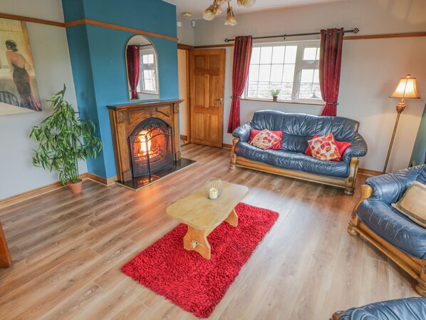 A living room with a fireplace, a blue leather sofa, a wooden coffee table, and a red rug. - Clodagh's Cottage (Collooney)
