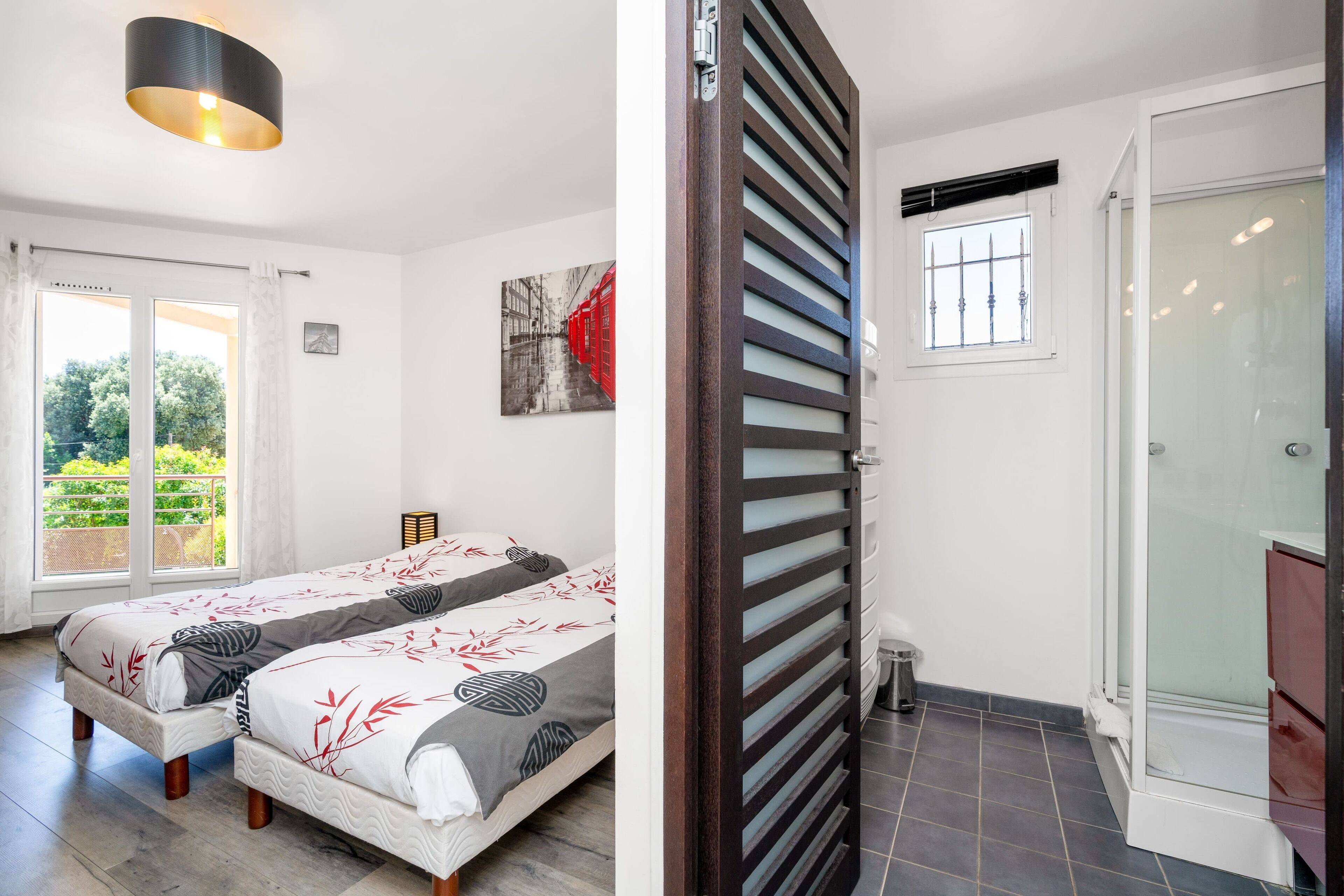 A bedroom with two beds, a large window, and a bathroom with a glass shower.