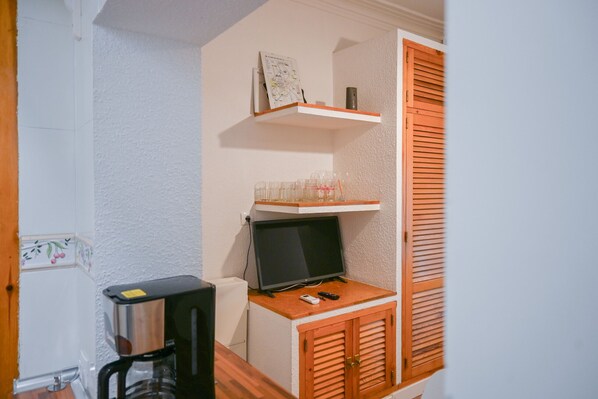 Una habitación pequeña con un armario de madera, un televisor y una cafetera.