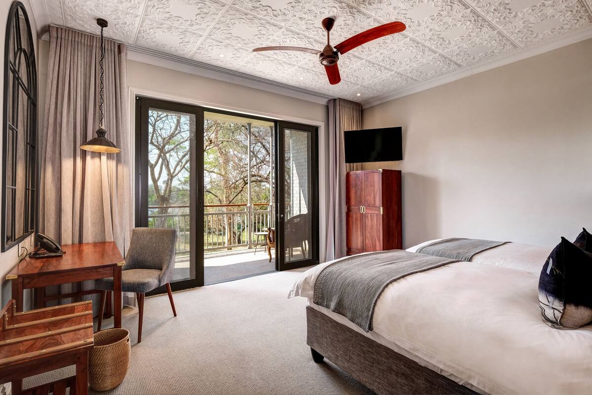 A hotel room with a large bed, a desk, a chair, a television, and a ceiling fan.