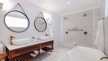 A modern bathroom with a freestanding bathtub, two sinks with round mirrors, and a shower area with a patterned tile wall.