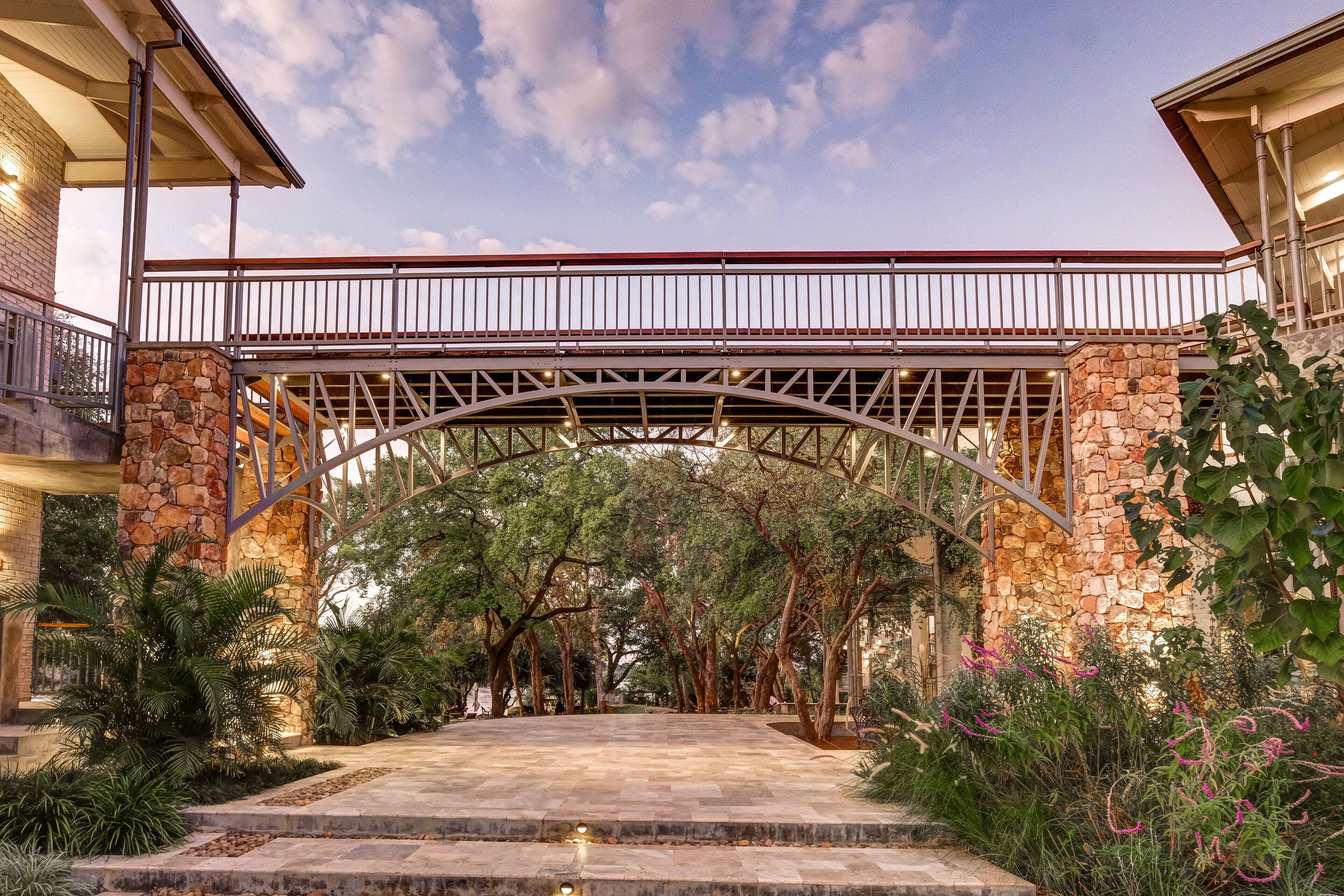 A covered walkway with stone pillars, surrounded by lush greenery and trees.