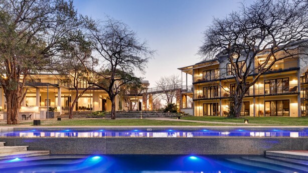 A modern hotel with a pool, outdoor seating, and a well-lit entrance. - Palm River Hotel (Victoria Falls)