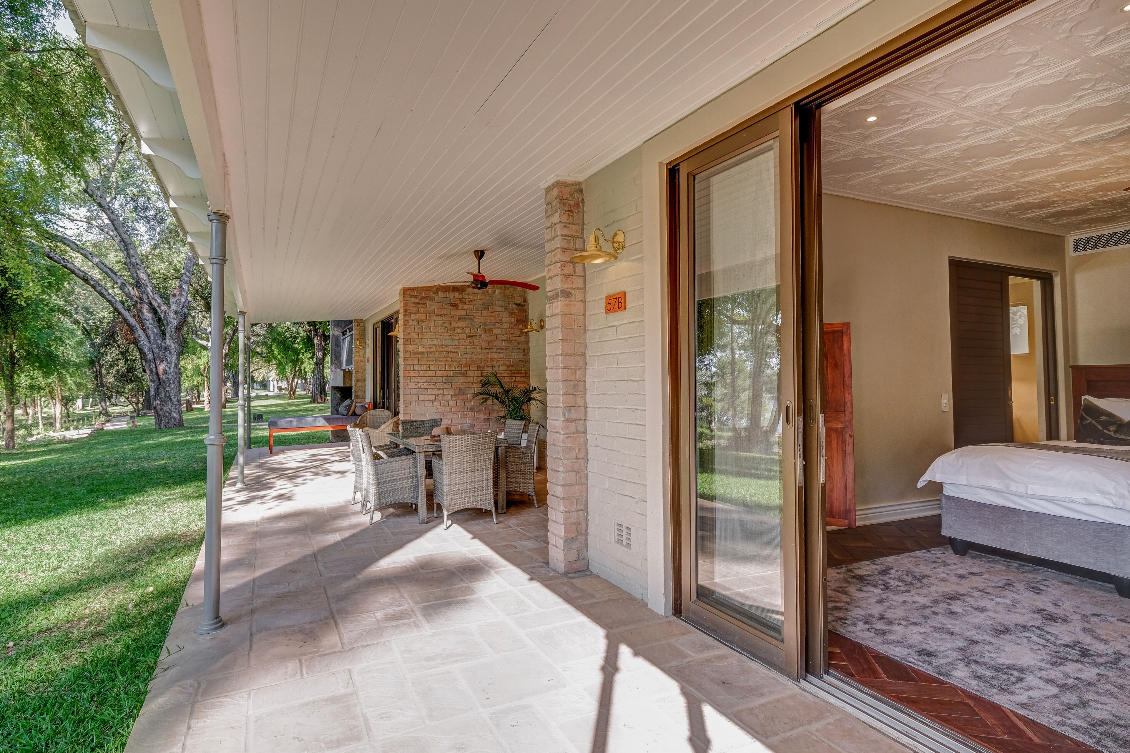 Een overdekt terras met een bakstenen muur, een eethoek en een slaapkamer met een grote schuifpui.