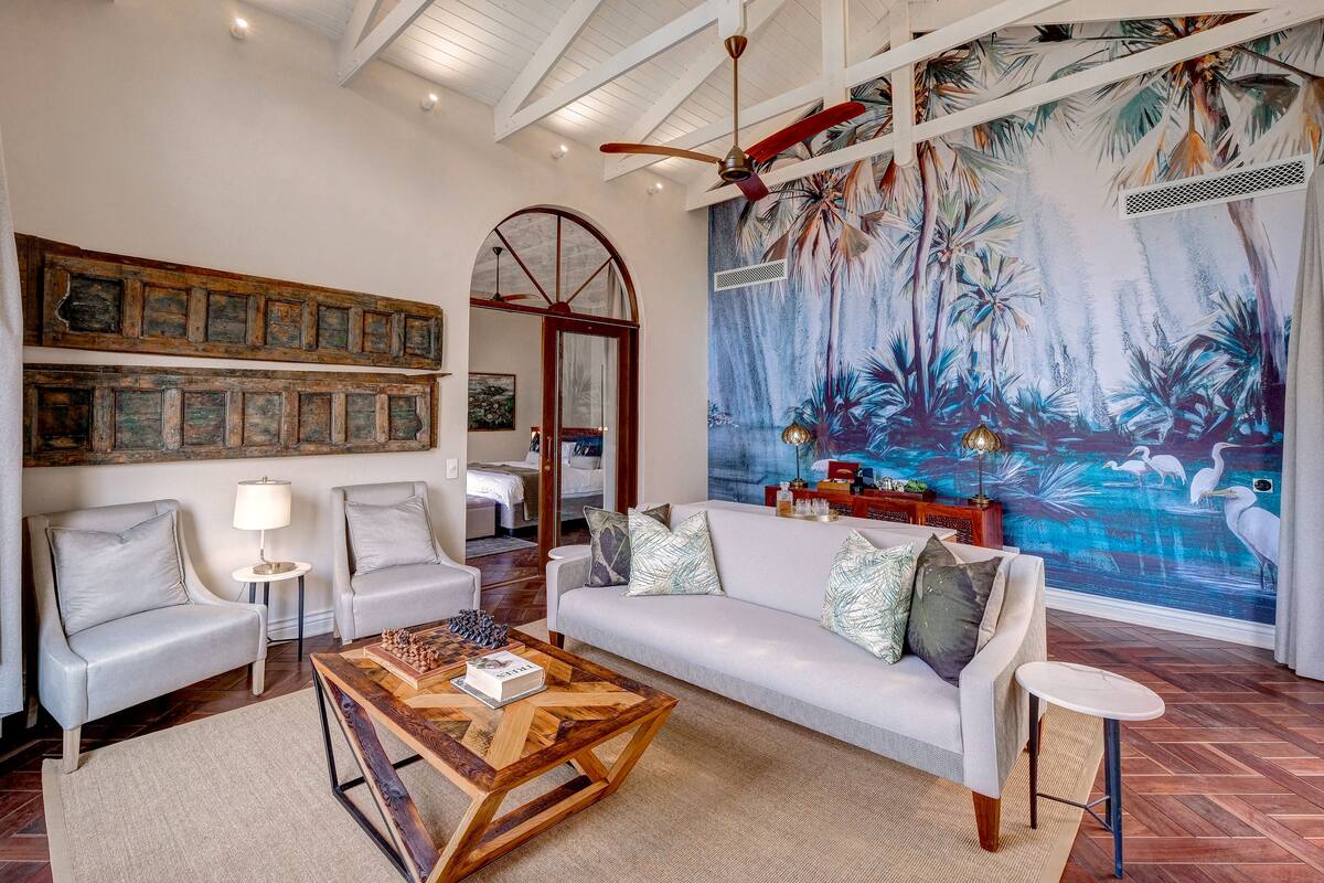 A spacious living room with a white sofa, a wooden coffee table, and a large mural of a tropical scene.