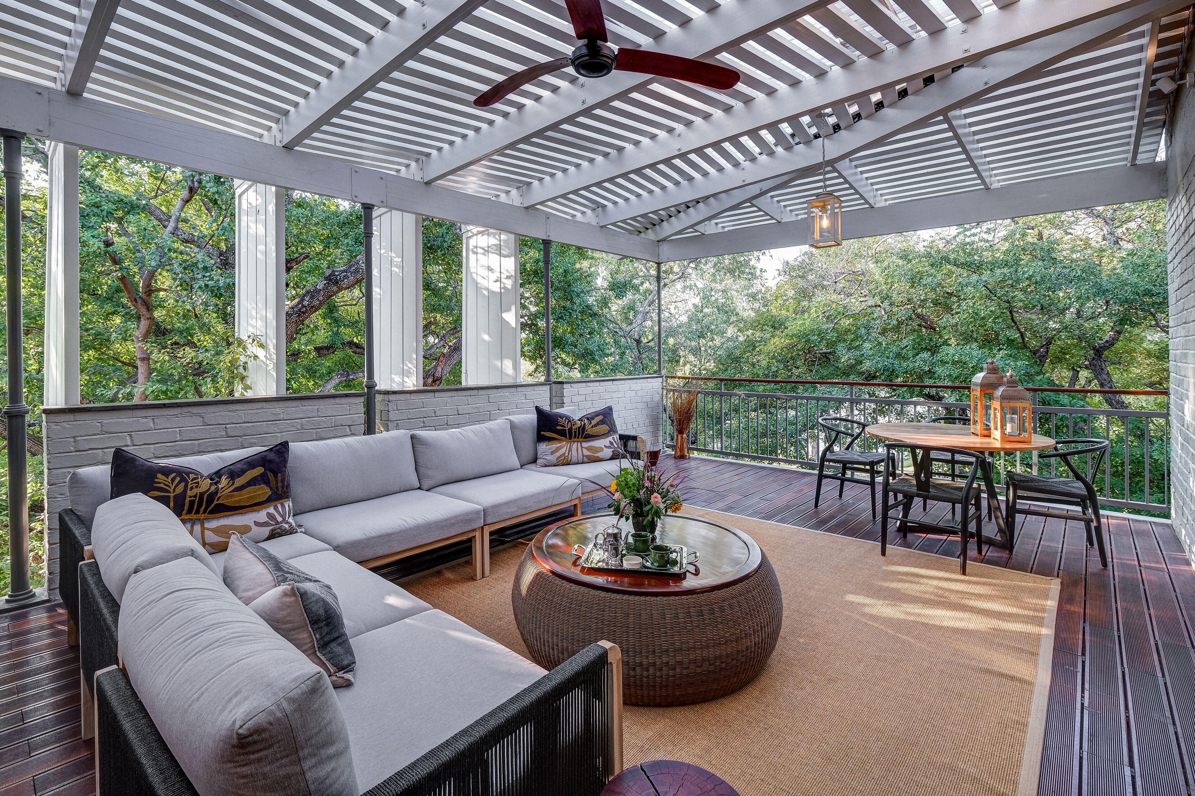 A covered outdoor seating area with a sofa, round table, and chairs, overlooking a lush garden.