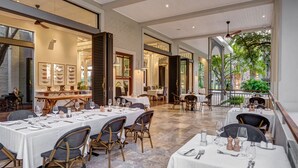A restaurant with outdoor seating, white tablecloths, and wicker chairs. - Palm River Hotel (Victoria Falls)