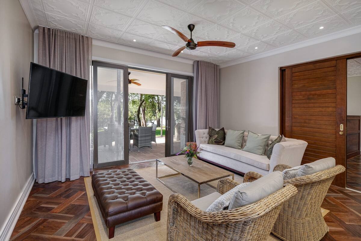 A modern living room with a flat-screen TV, a ceiling fan, a sofa, a coffee table, and a large window with curtains.