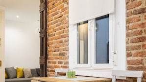 A room with a wooden table and chair, a brick wall, and a window with white blinds. - COZY APARTMENT IN THE NEIGHBORHOOD OF SALAMANCA JOG48 (Madrid)