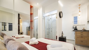 A modern hotel room with a large bed, a bathroom with a glass shower, a wooden dresser, and a large mirror. - COZY APARTMENT IN THE NEIGHBORHOOD OF SALAMANCA JOG48 (Madrid)